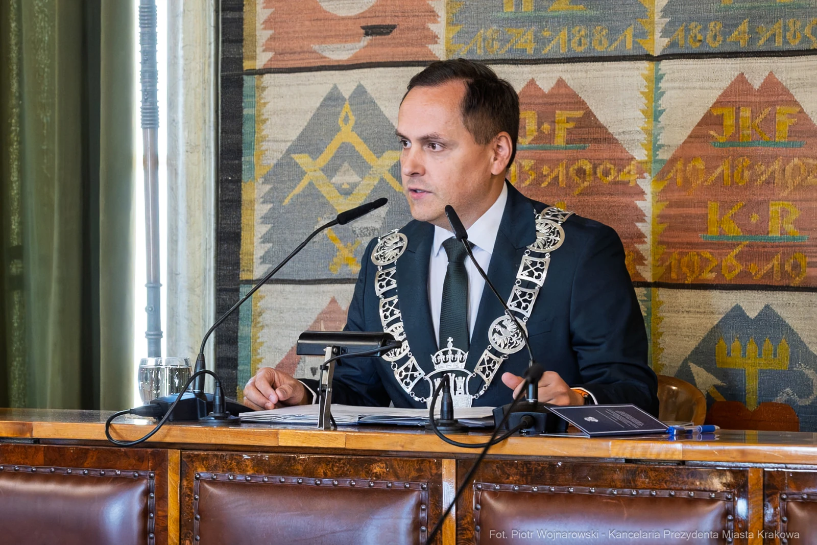 Mężczyzna w garniturze z łańcuchem na szyi przemawia podczas sesji w sali obrad.  Autor: Piotr Wojnarowski