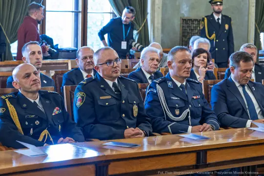 Grupa mężczyzn w mundurach oraz garniturach podczas uroczystości.
