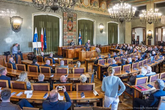Spotkanie w sali obrad z uczestnikami i mówcami przy stole prezydialnym.