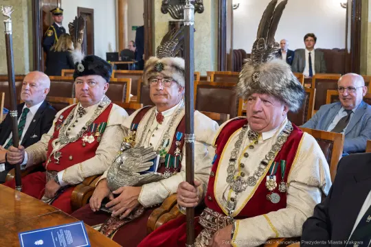 Czterech mężczyzn w tradycyjnych strojach z piórami, siedzących w sali obrad.