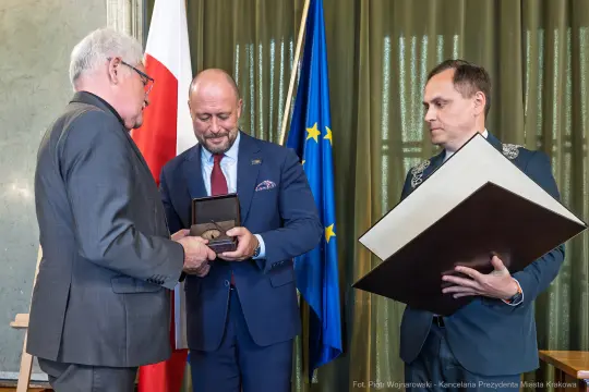 Wręczenie odznaczenia w obecności flagi Polski i Unii Europejskiej.