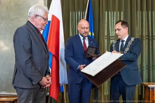 Wręczenie odznaczenia w obecności flagi Polski i Unii Europejskiej.