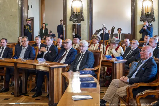 Uczestnicy uroczystości w sali obrad, wśród nich przedstawiciele władz i goście.