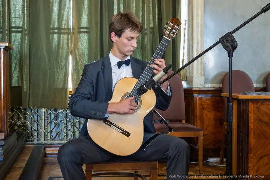 Młody mężczyzna gra na gitarze klasycznej w eleganckim stroju.