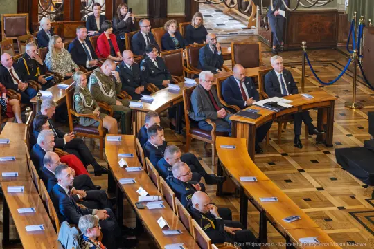 Uczestnicy uroczystości w sali obrad, w tym przedstawiciele władz i służb mundurowych.