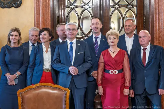 Grupa osób w formalnych strojach, pozująca w eleganckim wnętrzu.