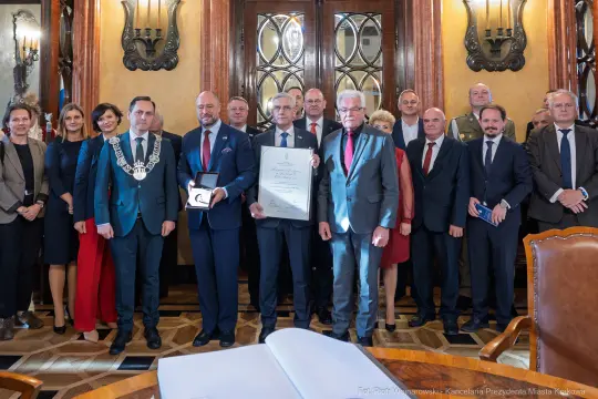 Uroczystość wręczenia nagrody w obecności wielu osób w eleganckim wnętrzu.