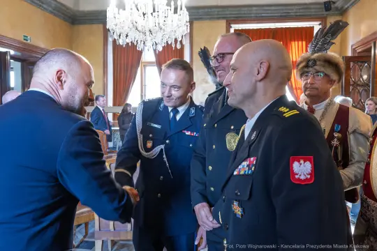 Mężczyźni w mundurach i garniturach rozmawiają w eleganckim wnętrzu.