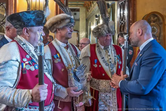 Mężczyźni w tradycyjnych strojach z insygniami rozmawiają w eleganckim wnętrzu.