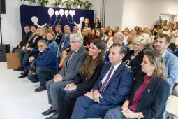 Grupa ludzi siedzących na sali podczas wydarzenia, z dekoracjami w tle.
