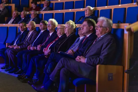Grupa osób siedzących na widowni, zwróconych w stronę sceny.