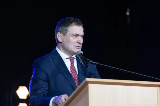 Mężczyzna w garniturze przemawia do mikrofonu przy mównicy.