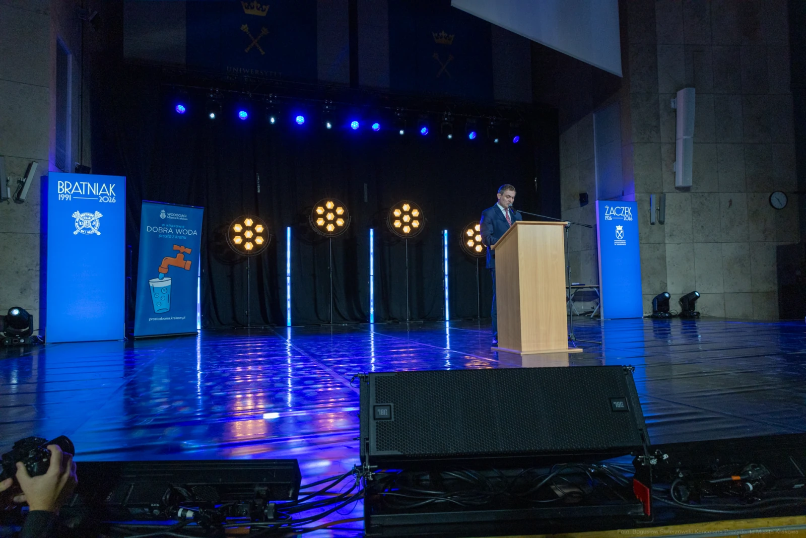 Mężczyzna przemawia z podium na tle oświetlonej sceny podczas wydarzenia.  Autor: Bogusław Świerzowski