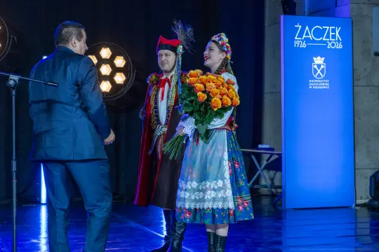 Mężczyzna i kobieta w tradycyjnych strojach ludowych, wręczający bukiet róż.