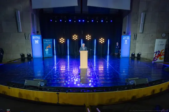 Mężczyzna przemawia z podium na scenie oświetlonej reflektorami.