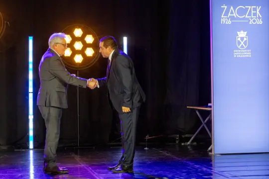 Dwaj mężczyźni uścisnęli sobie dłonie na tle dekoracji sceny.
