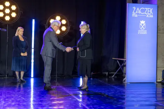 Uroczystość wręczenia nagrody, dwie osoby podają sobie ręce, w tle logo uczelni.