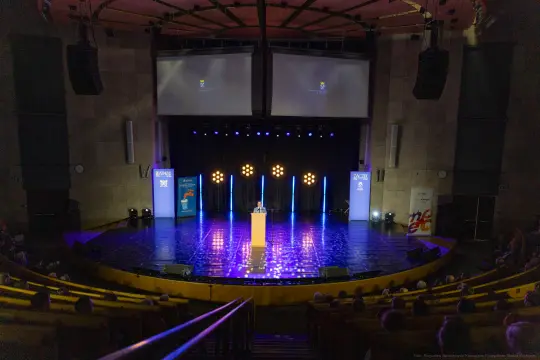 Scena z podium, oświetlona reflektorami, z widownią w tle.