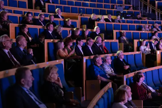 Widownia wypełniona ludźmi siedzącymi na niebieskich fotelach.