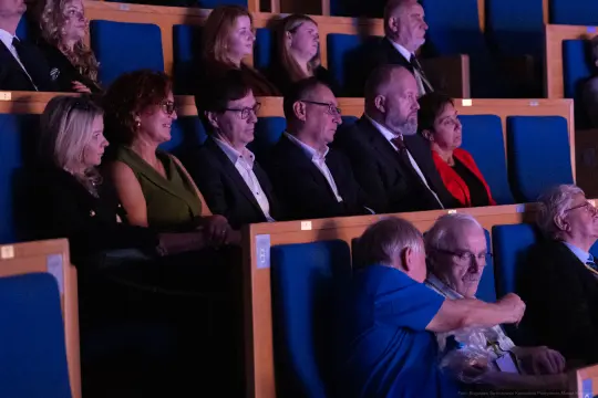 Grupa ludzi siedzących na widowni w teatrze, skupionych na wydarzeniu.