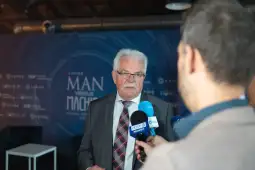 Mężczyzna w garniturze udziela wywiadu, w tle logo wydarzenia.