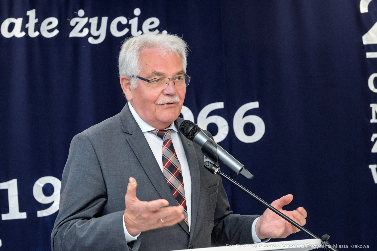Mężczyzna w garniturze przemawia do mikrofonu na tle niebieskiego tła z napisami.  Autor: Piotr Wojnarowski