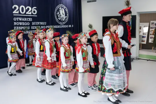 Dzieci w tradycyjnych strojach ludowych podczas uroczystości otwarcia nowego budynku.