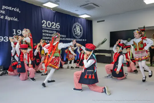 Dzieci w tradycyjnych strojach ludowych tańczą na scenie.