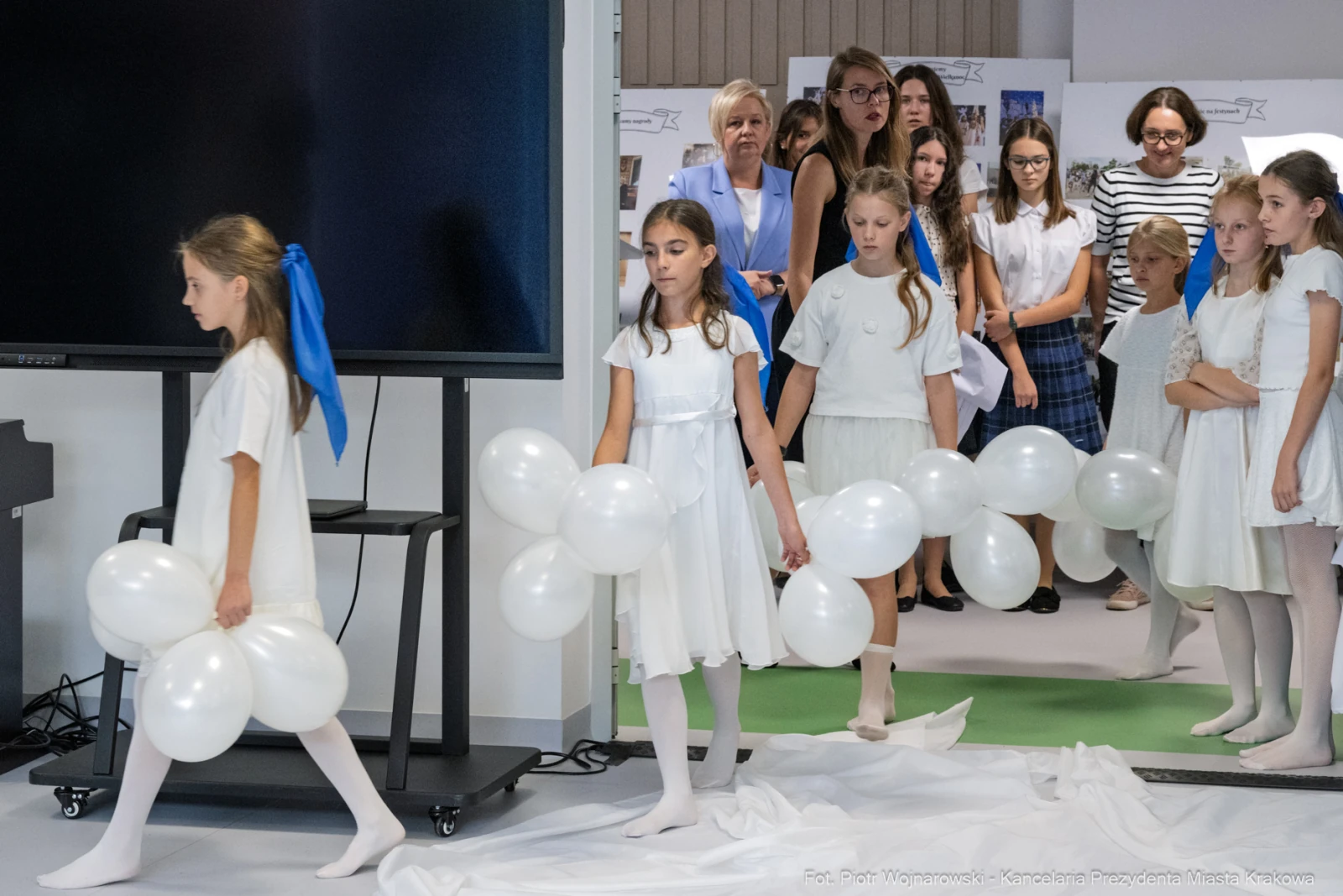 Dziewczynki w białych sukienkach niosą balony, podczas wydarzenia w tle widoczni dorośli.  Autor: Piotr Wojnarowski