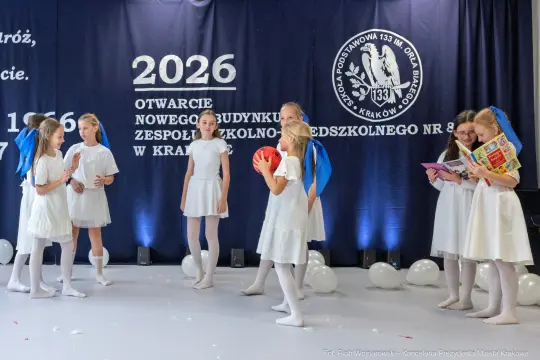 Uczniowie w białych strojach na scenie podczas otwarcia nowego budynku szkoły.