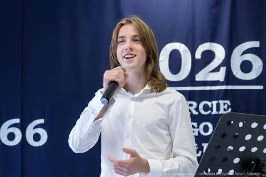 Młody chłopak śpiewa do mikrofonu na tle niebieskiej ściany.
