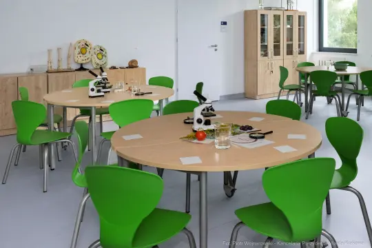 Nowoczesna sala lekcyjna z zielonymi krzesłami i stołami, wyposażona w mikroskopy.
