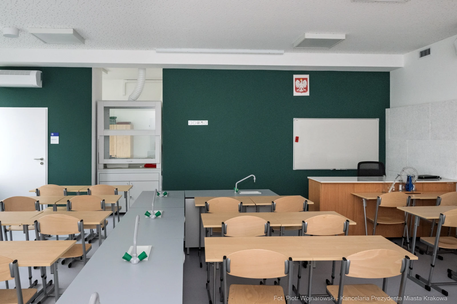 Pusta sala lekcyjna z zieloną ścianą, biurkiem nauczyciela i rzędem stołów.  Autor: Piotr Wojnarowski