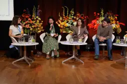Panel dyskusyjny z czterema osobami, kwiaty w tle, mikrofon w ręku jednej z uczestniczek.