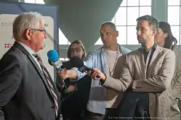 Konferencja prasowa z udziałem mężczyzny udzielającego wywiadu oraz reporterów.