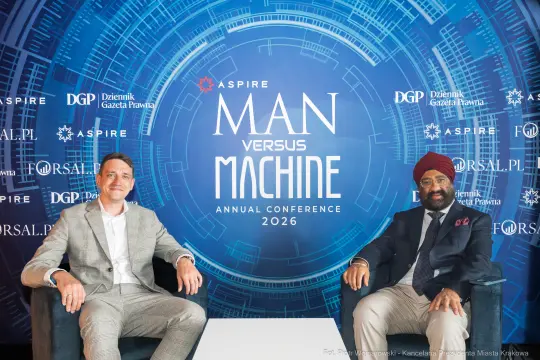 Dwóch mężczyzn siedzących na kanapie przed tłem konferencji Man versus Machine 2026.