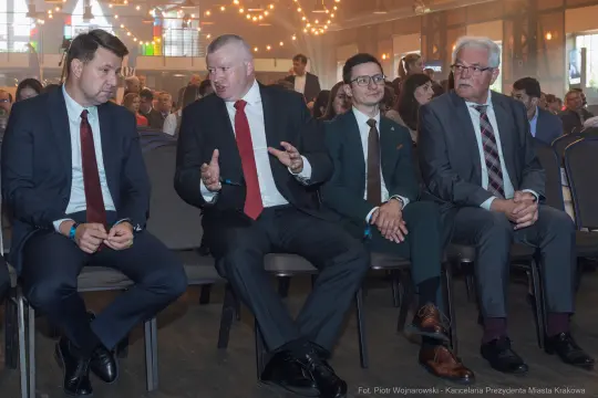Czterech mężczyzn w garniturach siedzących przy stole, rozmawiających ze sobą.