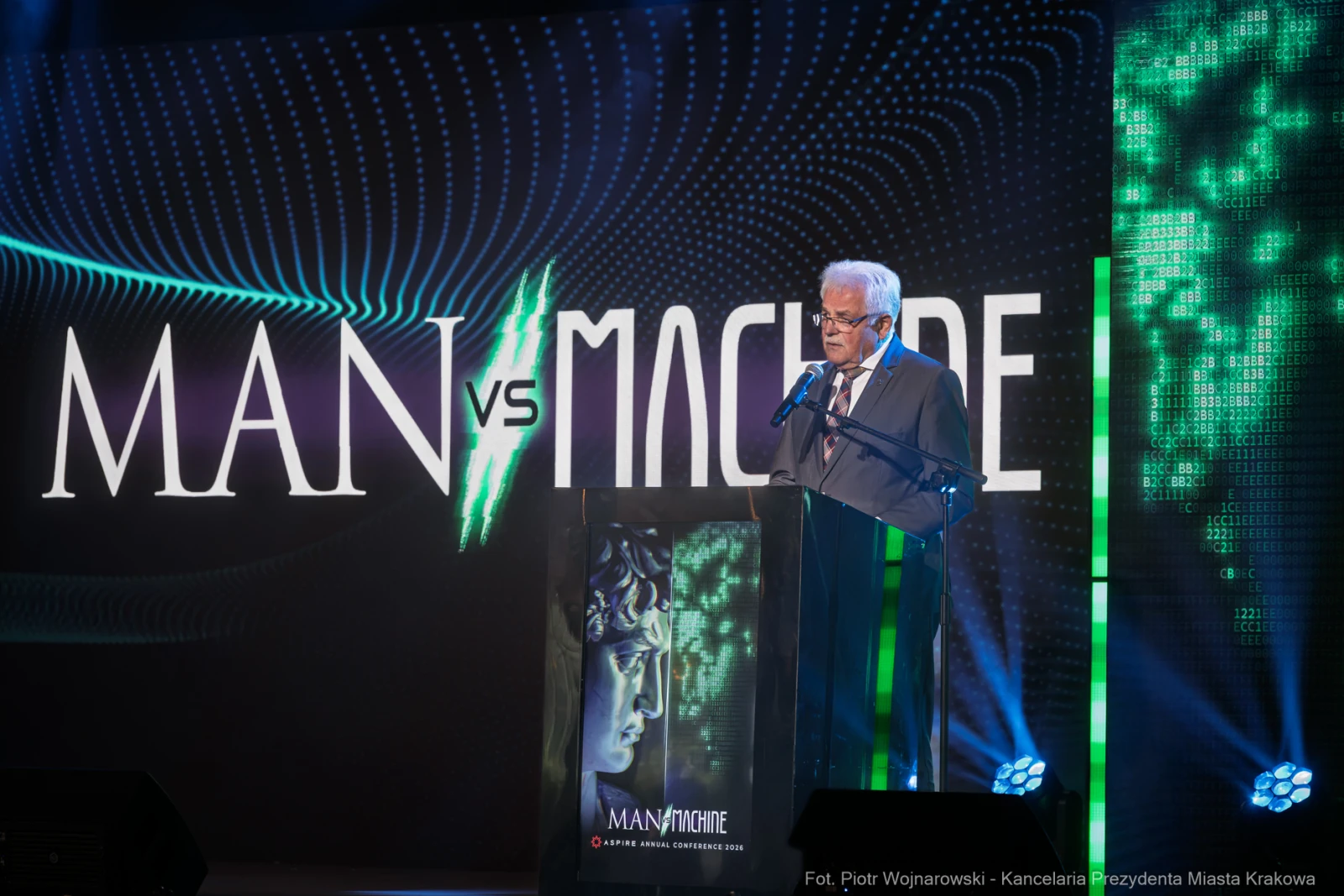Mężczyzna przy mównicy podczas konferencji, z tłem z napisem Man vs Machine.  Autor: Piotr Wojnarowski