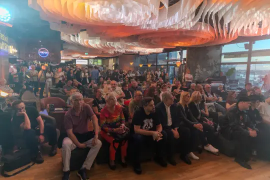 Tłum ludzi siedzących w lokalu, skupionych na wydarzeniu.