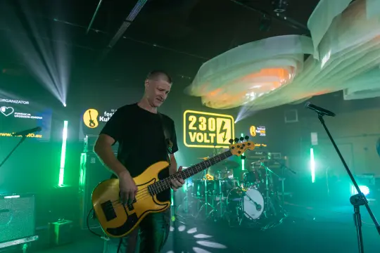 Muzyk grający na gitarze basowej podczas koncertu z efektami świetlnymi.