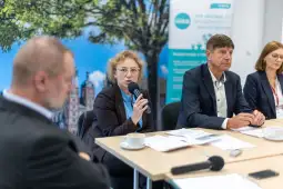 Panel dyskusyjny z uczestnikami przy stole, jeden z mówców trzyma mikrofon.