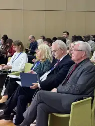 Grupa ludzi siedzących na konferencji, skupionych na prezentacji.
