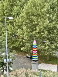 Kolorowy obelisk w paski w otoczeniu zieleni drzew.