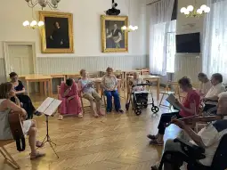 Spotkanie muzyczne w sali, uczestnicy słuchają występu gitarzystki.
