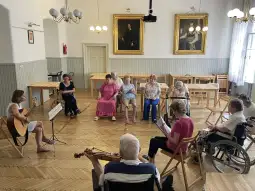 Grupa osób starszych uczestniczy w zajęciach muzycznych w sali z instrumentami.