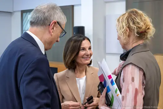 Trzy osoby rozmawiają w biurze, jedna z nich trzyma dokumenty.