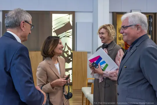 Cztery osoby rozmawiają w biurze, jedna z nich trzyma dokumenty.
