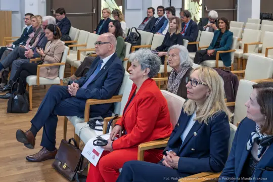 Grupa osób siedzących w sali konferencyjnej, uczestniczących w spotkaniu.