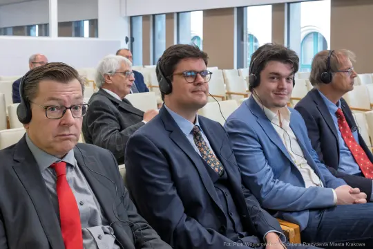 Czterech mężczyzn w słuchawkach siedzi na sali konferencyjnej.