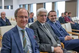 Trzech mężczyzn w garniturach siedzących w sali konferencyjnej.